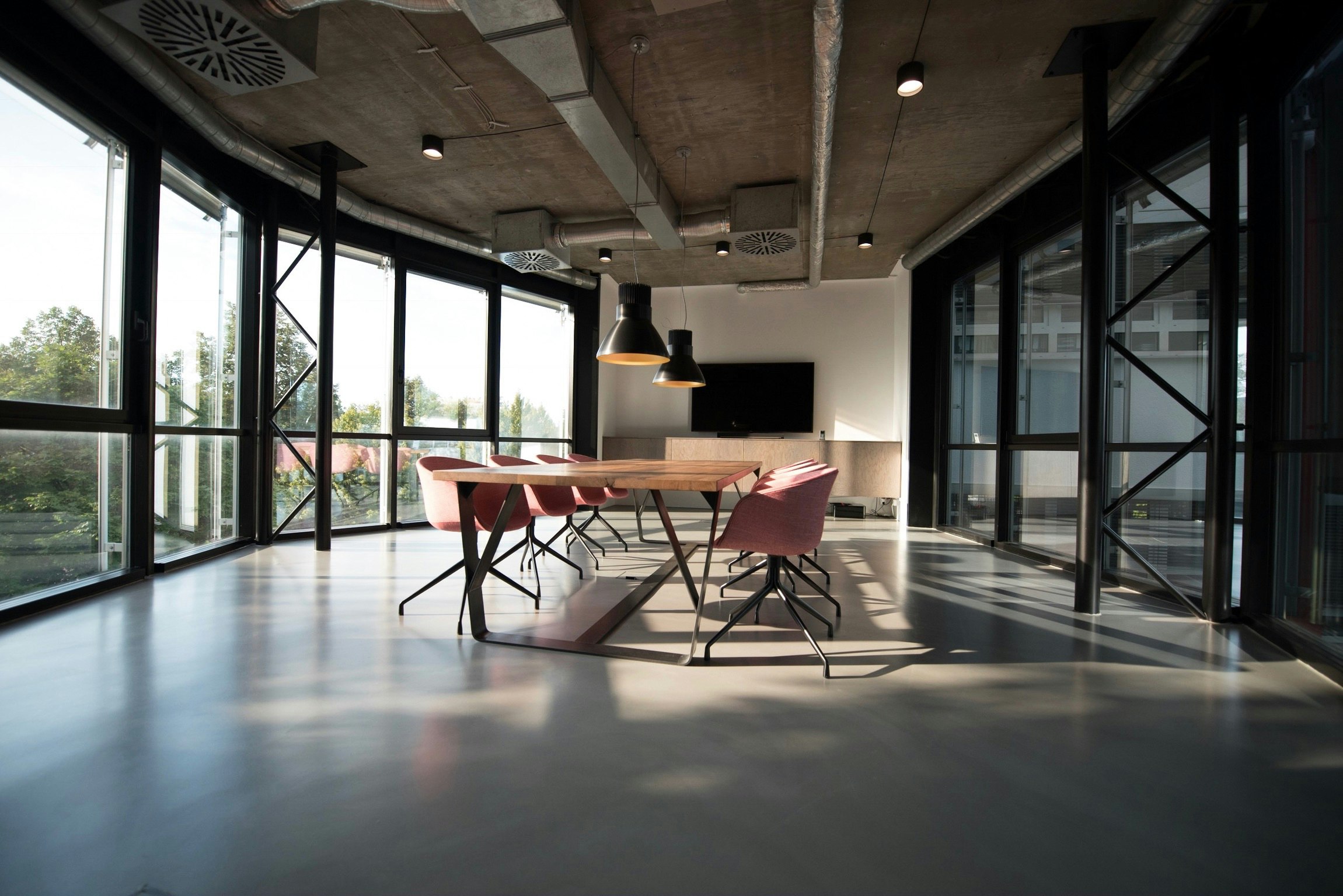 A bright open-plan coworking hall with tall windows and long shared tables
