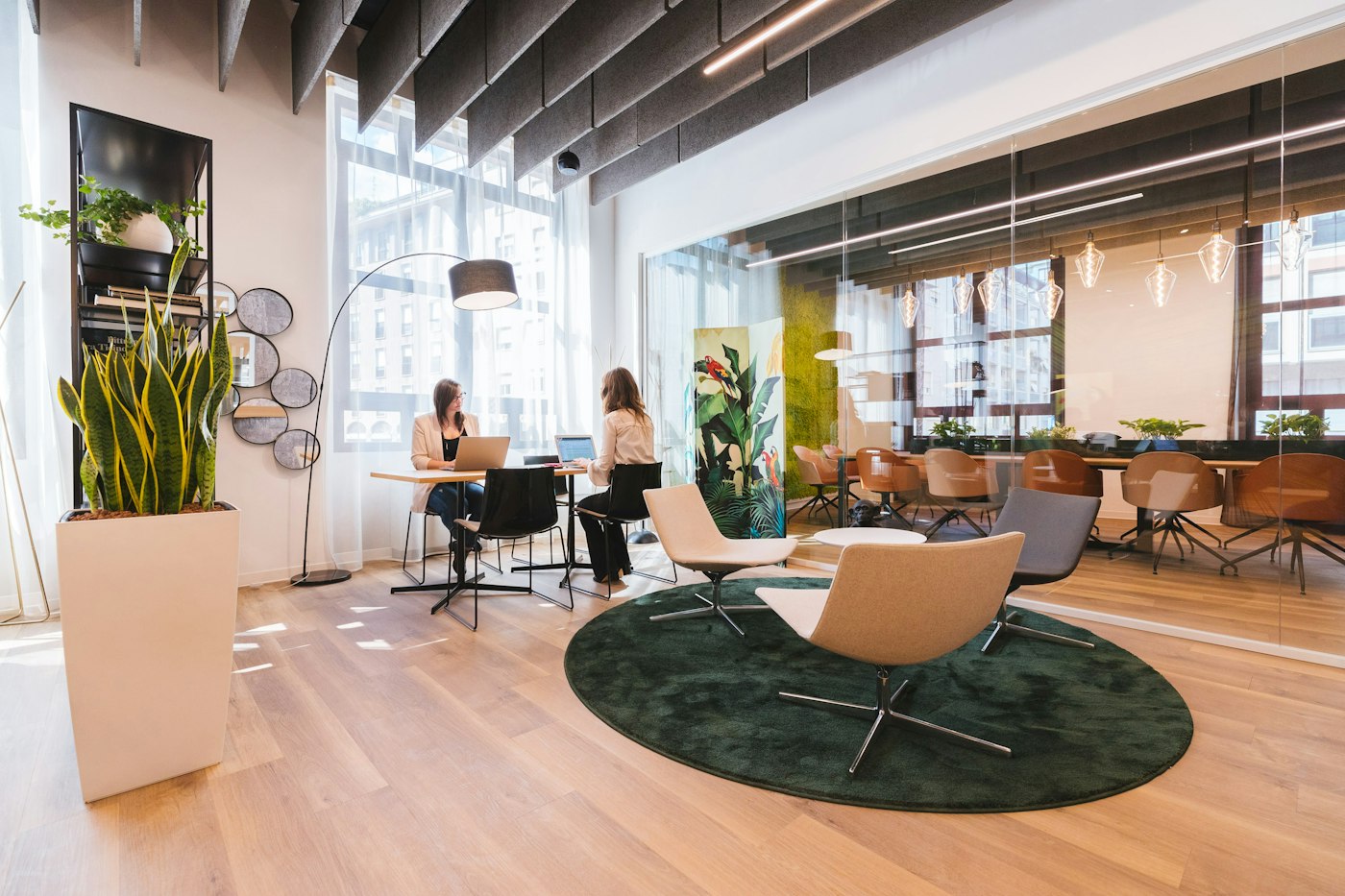 A sunny coworking lounge with armchairs, plants and people at work